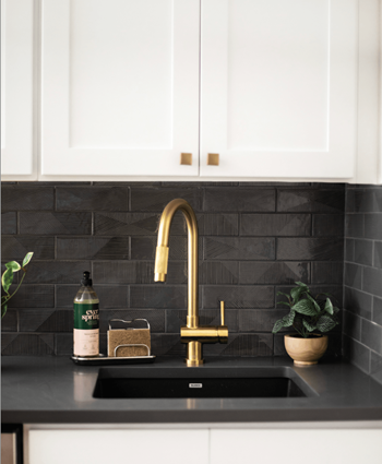 a kitchen sink with a gold faucet and white cabinets