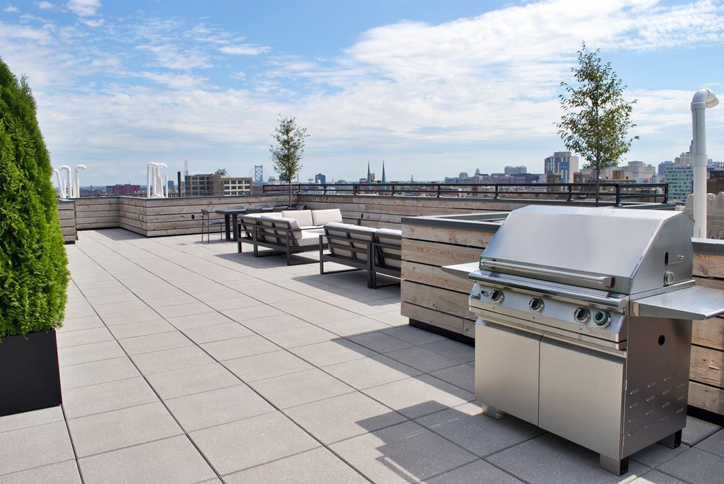 a barbecue grill on a rooftop patio with a city in the background