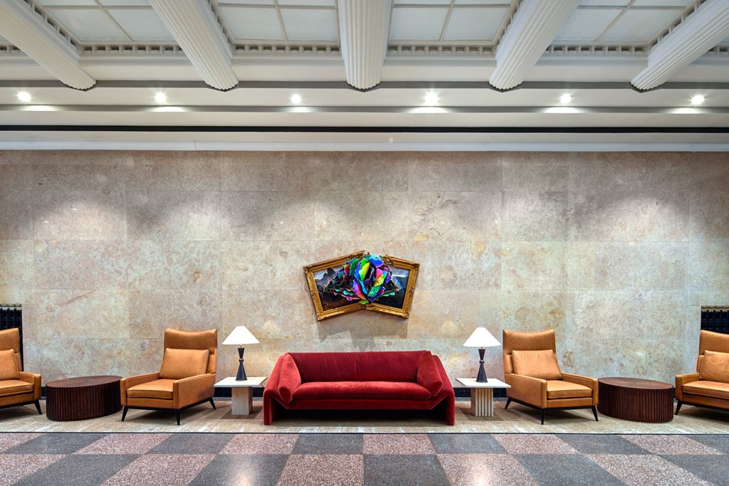 A room with a red couch and chairs with a painting hanging on the wall.