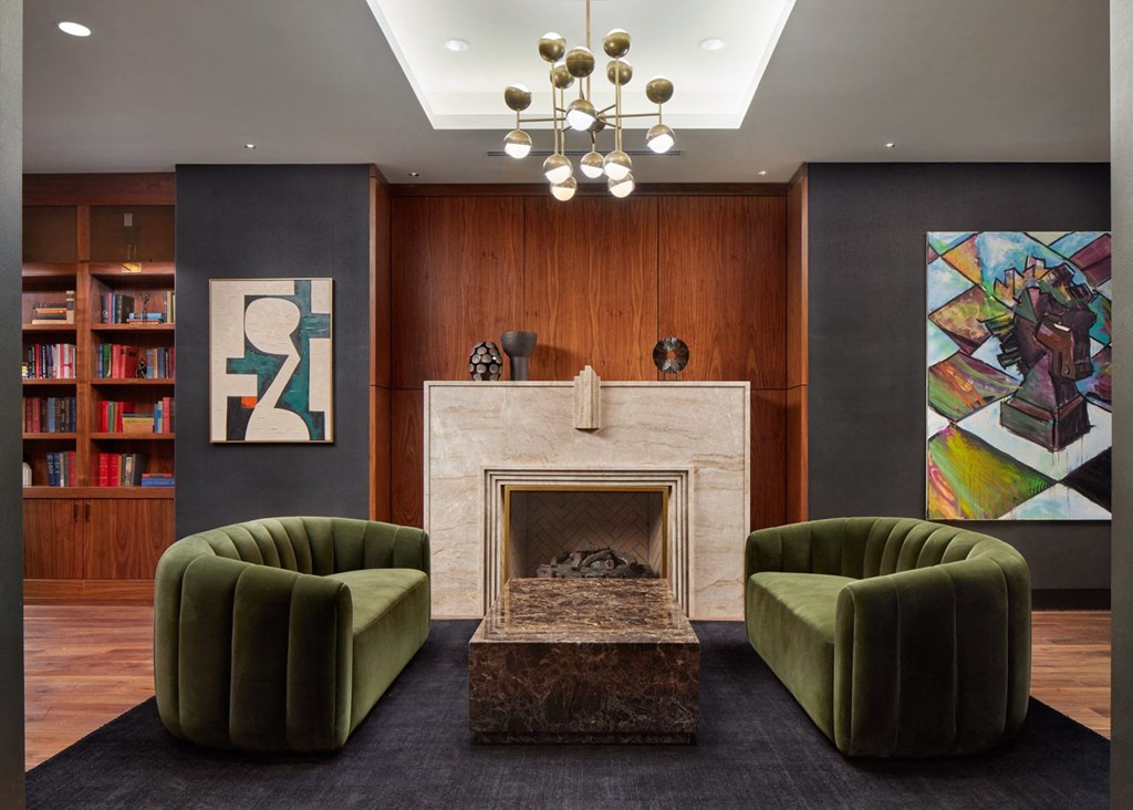 A living room with a fireplace, two green chairs, and a bookshelf.