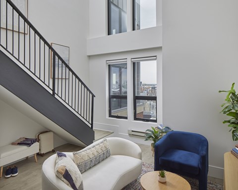 A living room with a white couch, a blue chair, and a small table with a plant on it.