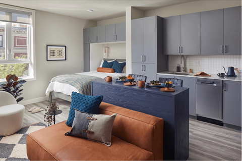 A snapshot of a LVL West studio apartment floorplan with a bed by a large window,  a kitchen, bar seating dining area, and a couch and armchair in the living area.