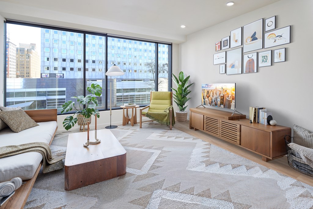 A living room with a large window, a white sofa, a wooden coffee table, and a rug with a geometric pattern.