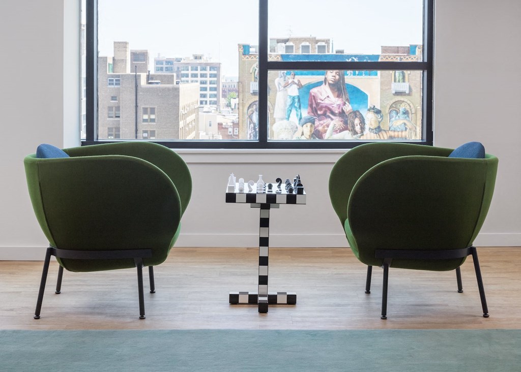 a living room with green chairs and a chess board in front of a window