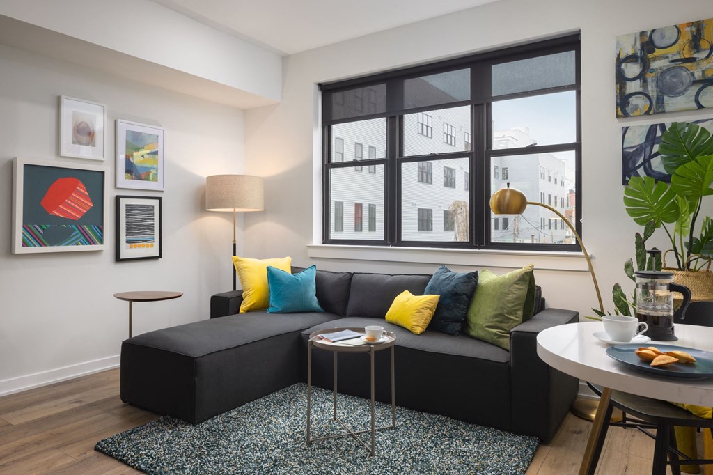 a living room with a black couch and yellow and blue pillows