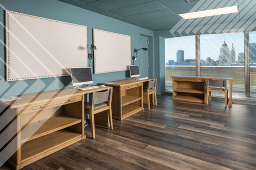 A room with wooden desks and chairs, a whiteboard, and a laptop on one of the desks.
