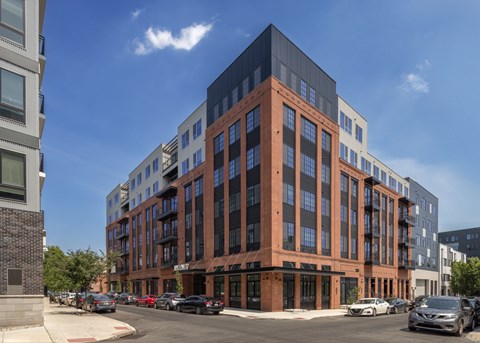 A modern multi-story building with a brick facade is surrounded by parked cars.