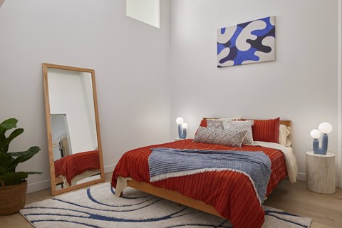 A bedroom with a red bedspread and a blue and white abstract painting on the wall.