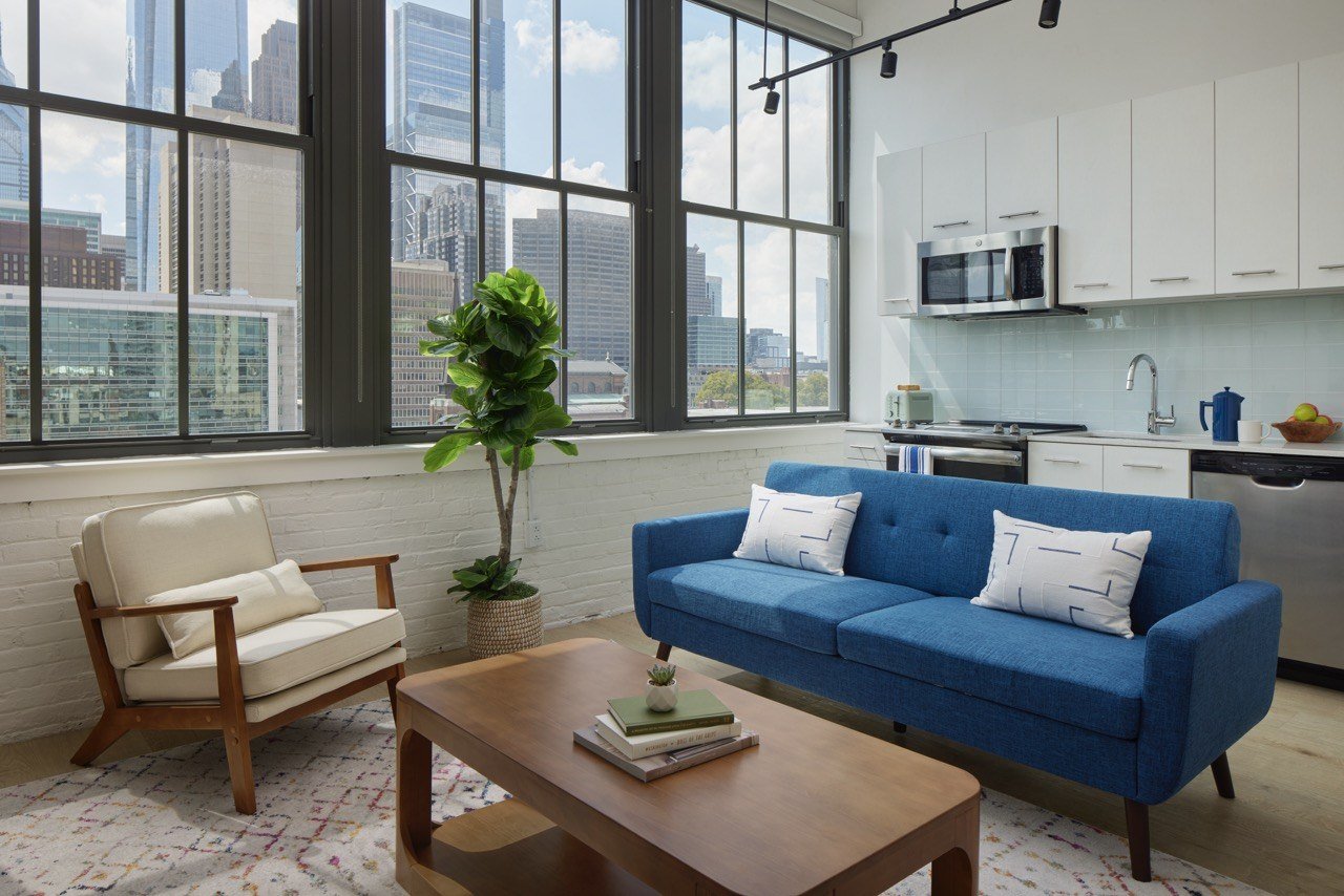 A blue couch with white pillows sits in a living room with a view of the city.