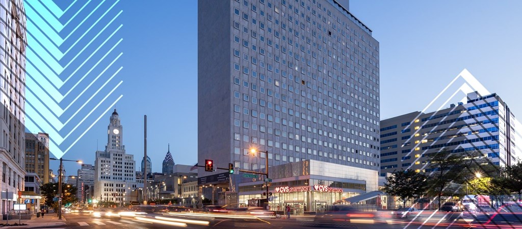 A city street at dusk with cars passing by and buildings in the background.