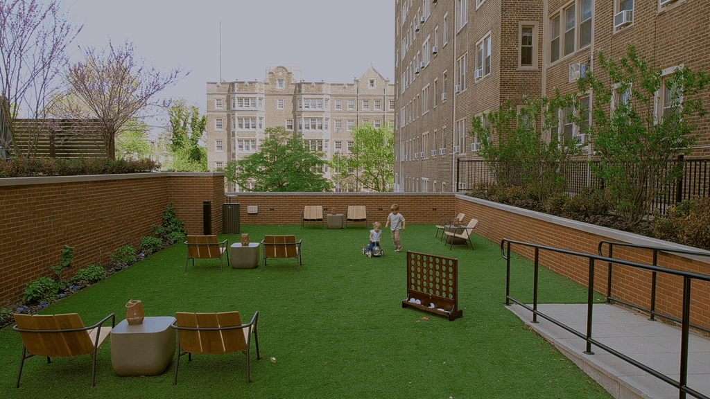 A man is standing in a courtyard with a green lawn and a brick wall.