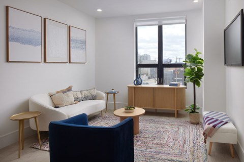 A living room with a white couch, a blue chair, a wooden cabinet, and a flat screen TV mounted on the wall.
