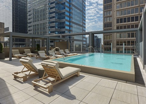 A pool with sun loungers on a balcony overlooking a city.