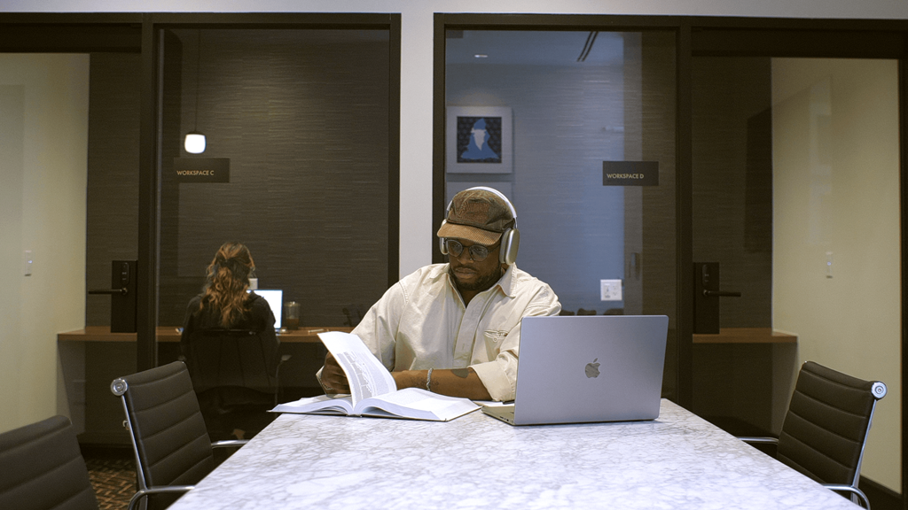 A man in a white shirt is sitting at a table with a laptop and a book.