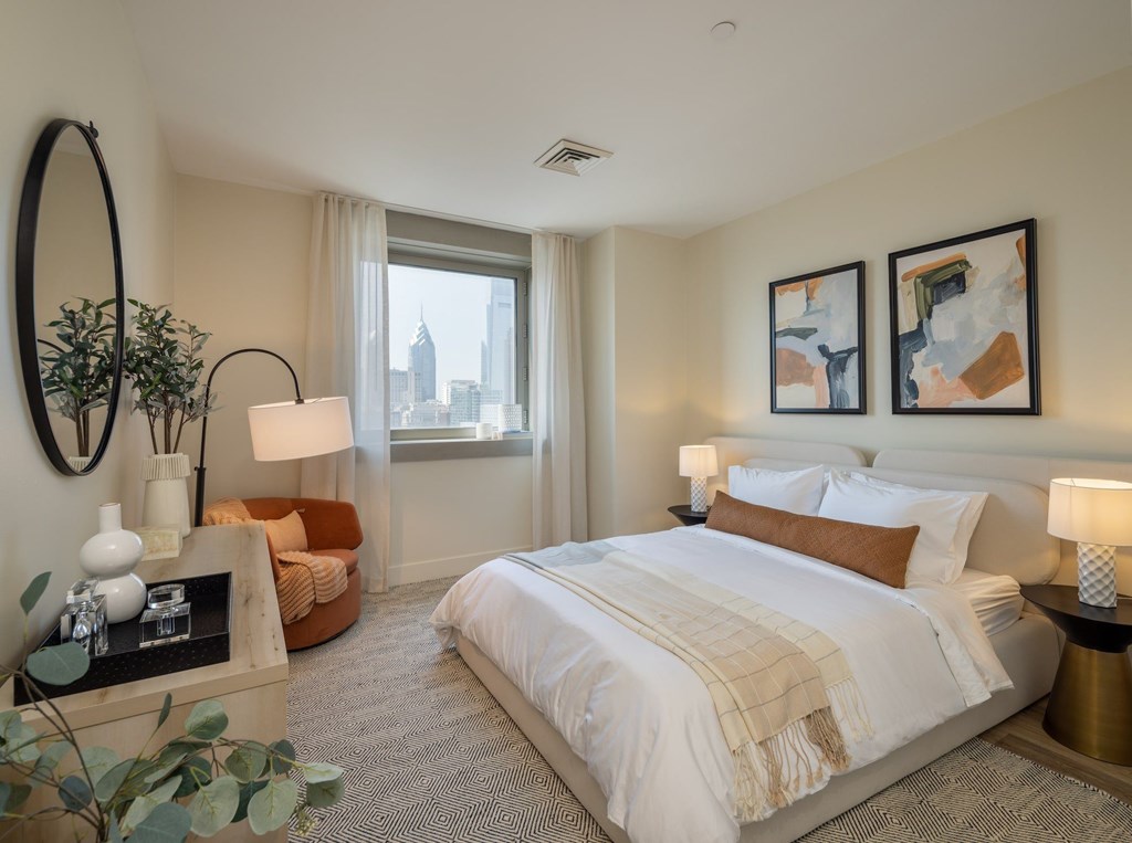 A bedroom with a large bed, a round mirror, and a view of the city.