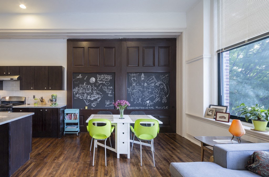 a living room with a table and chairs in front of a chalkboard