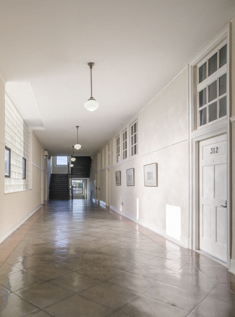 a long hallway with white walls and windows and a concrete floor