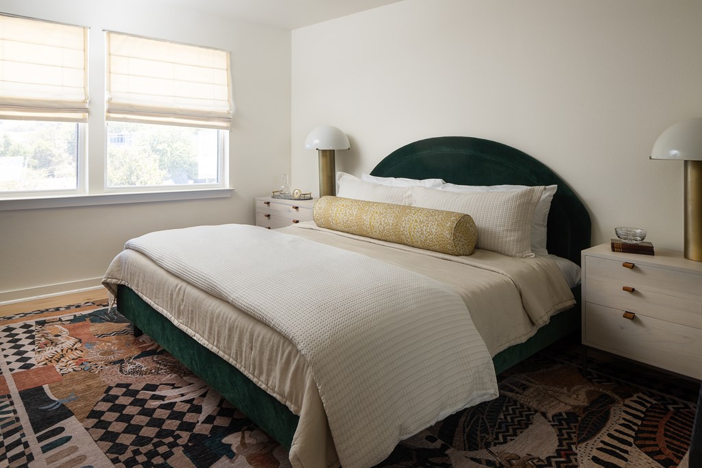 A bedroom with a large bed and a patterned rug at The PARKER on E Mulberry Apartments, Texas