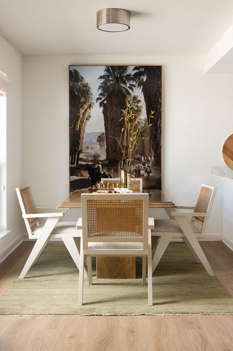 A dining room with a table set for two and a large painting of a palm tree in the background at The PARKER on E Mulberry Apartments, Texas