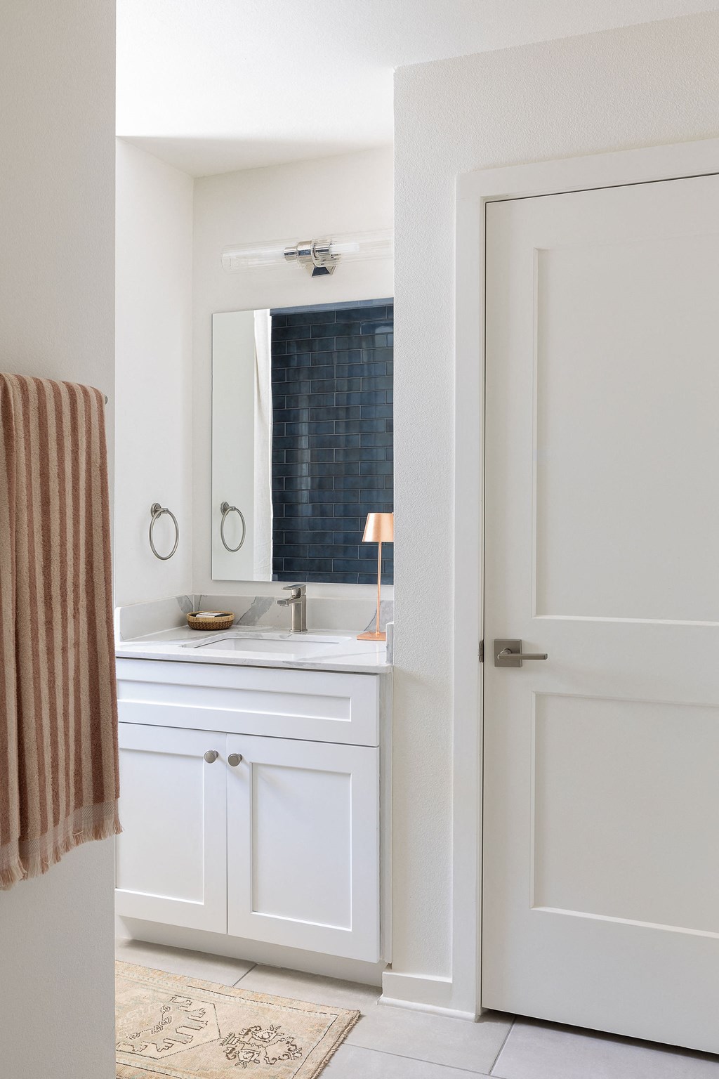 A bathroom with a white door and a white sink with a brown towel hanging on the wall at The PARKER on E Mulberry Apartments, San Antonio, TX, 78209