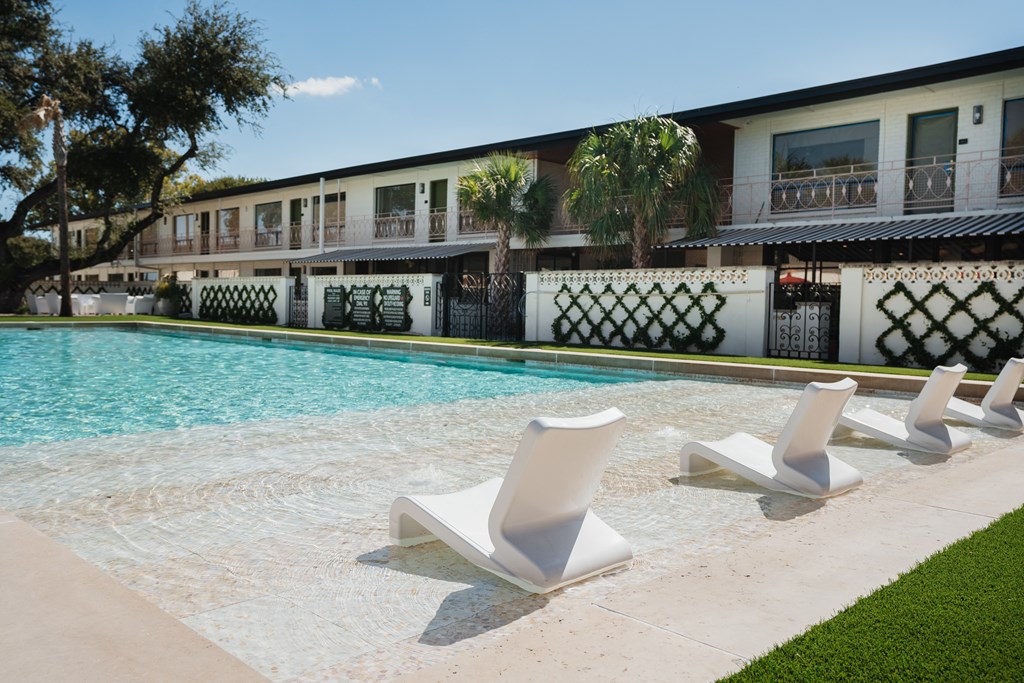 A row of white lounge chairs are arranged on the edge of a pool at The PARKER on E Mulberry Apartments, San Antonio, 78209