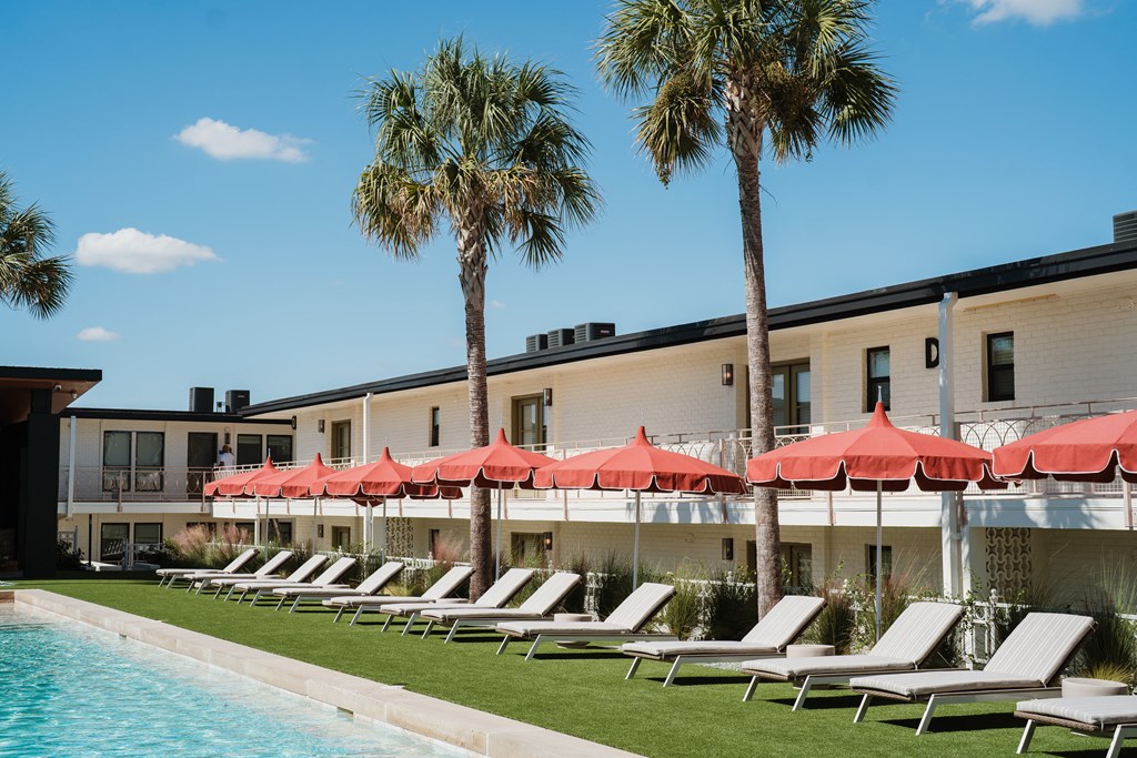A row of lounge chairs are set up under red umbrellas on a lawn at The PARKER on E Mulberry Apartments, San Antonio