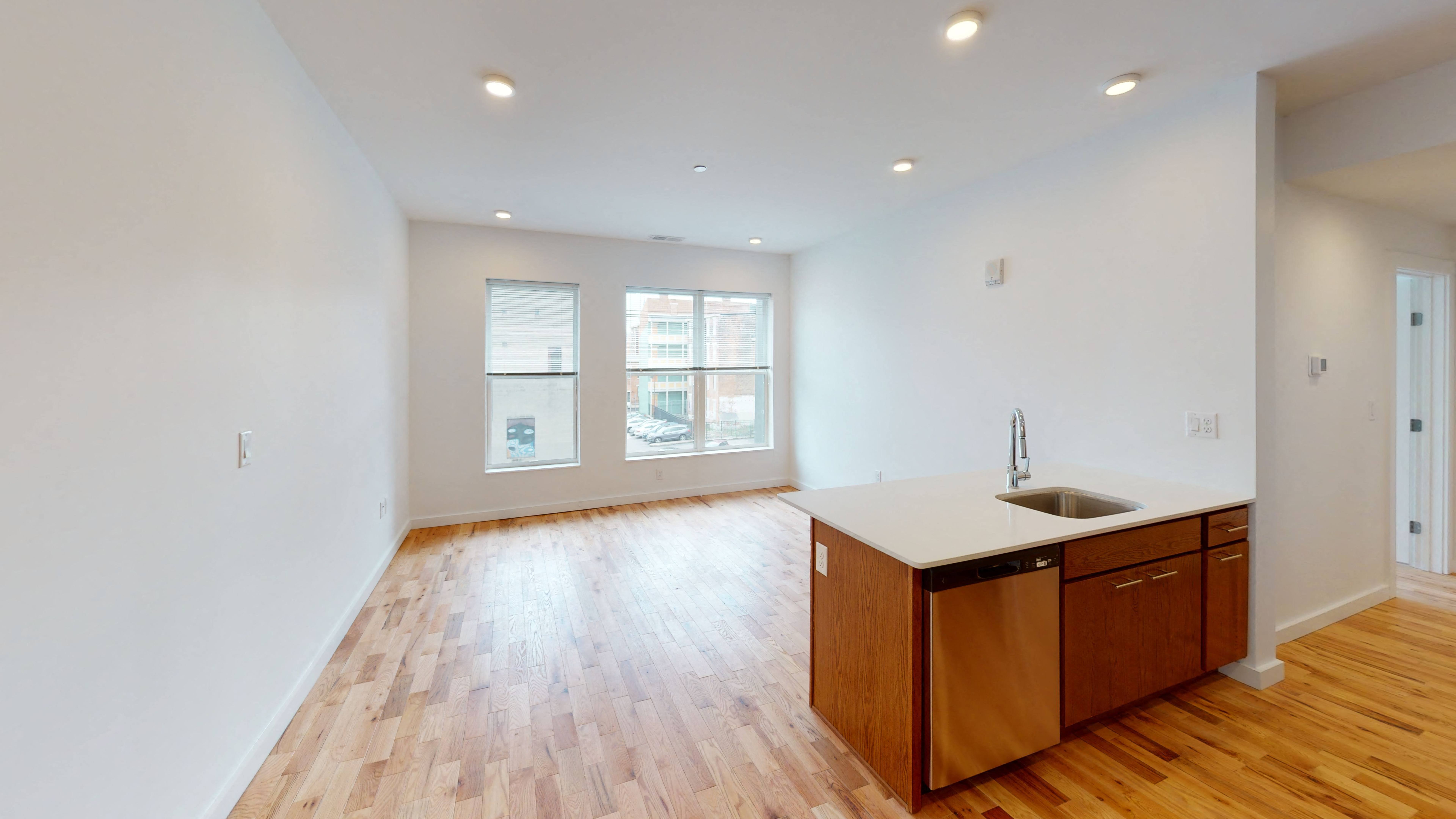an empty living room and kitchen with wood flooring and a sink