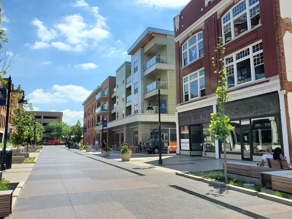 a city street with buildings and people sitting on benches