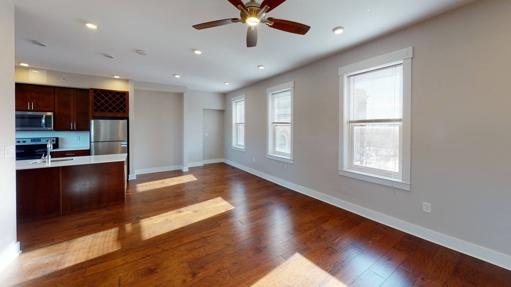an empty living room with a ceiling fan and a kitchen