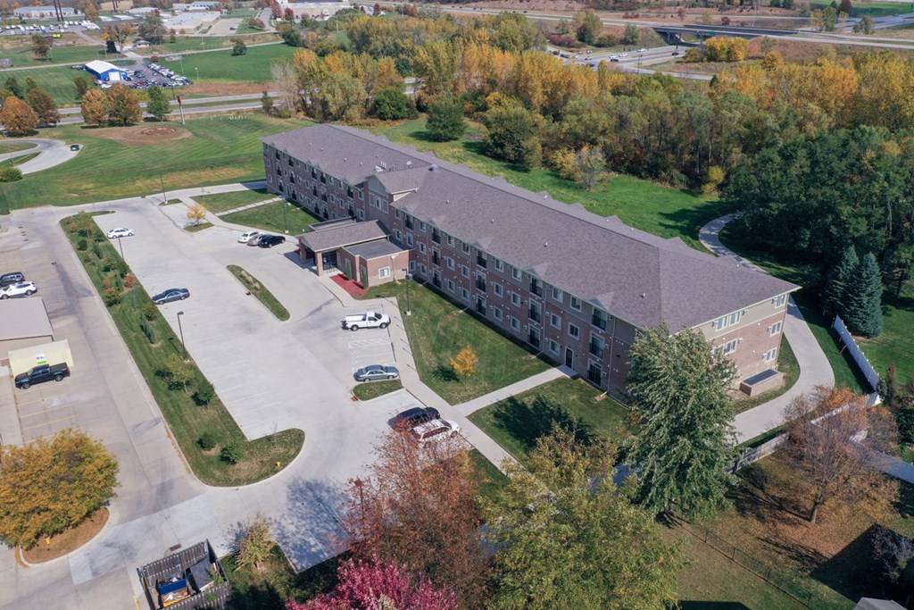 an aerial view of a large brick building with a gray roof and a parking lot with cars