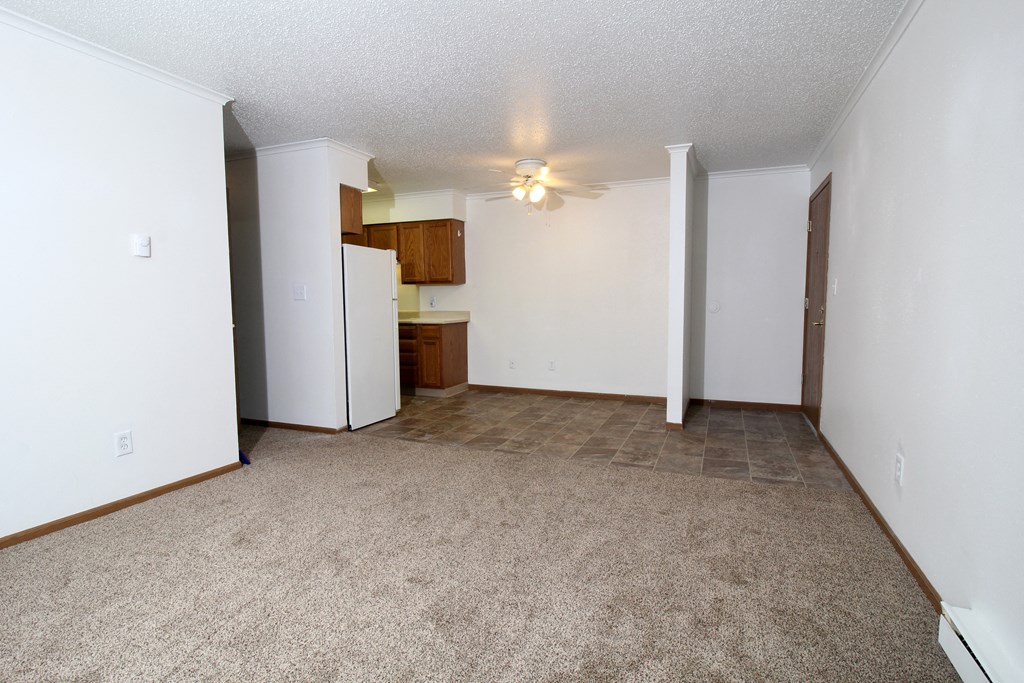 an empty living room with a kitchen in the background