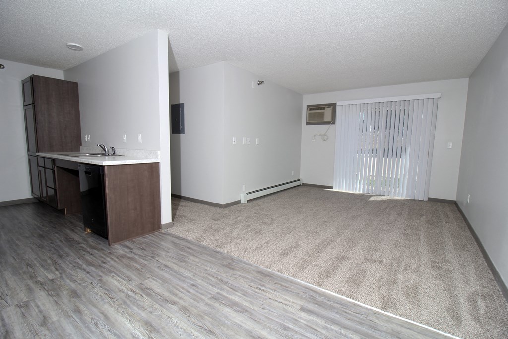 an empty living room with a kitchen in the background