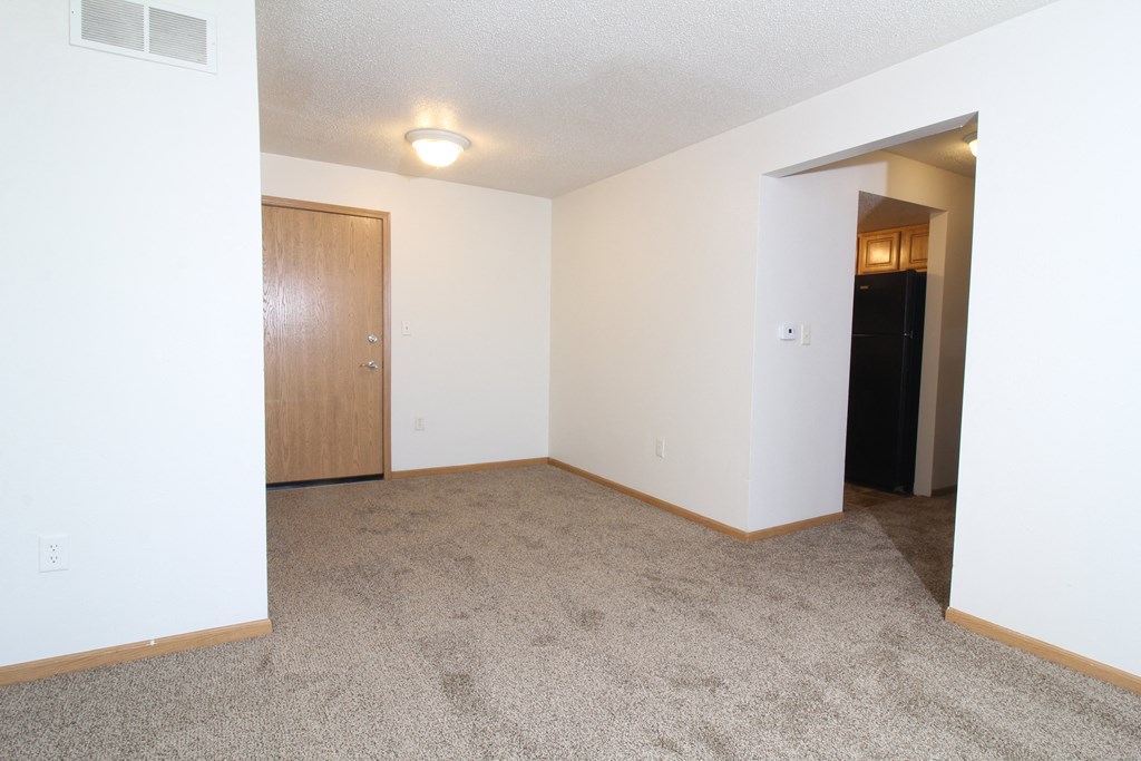 an empty living room with a door to a hallway and a carpeted floor
