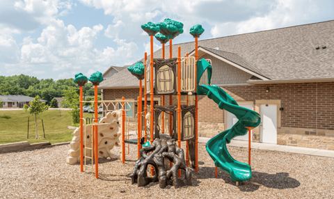 A playground with a green slide and orange climbing structures.