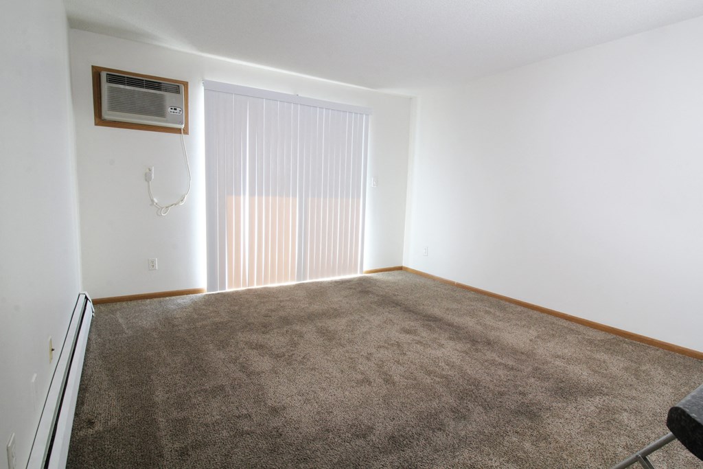 an empty room with a carpeted floor and a white wall with a white air conditioner