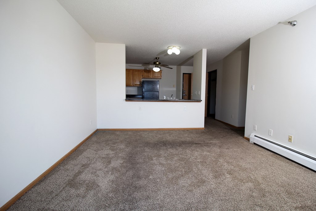 an empty living room with a kitchen in the background