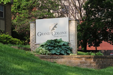 A sign for Grand Colony Apartments is displayed in front of a building.