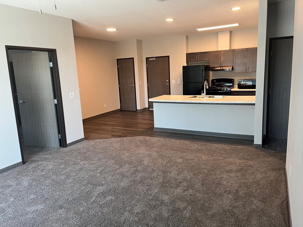 an empty living room with a kitchen and a door to a closet