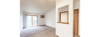 A large, empty room with a carpeted floor and a window with blinds.