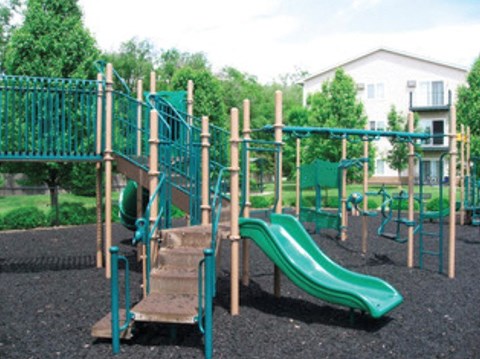 A playground with a green slide and a wooden climbing frame.