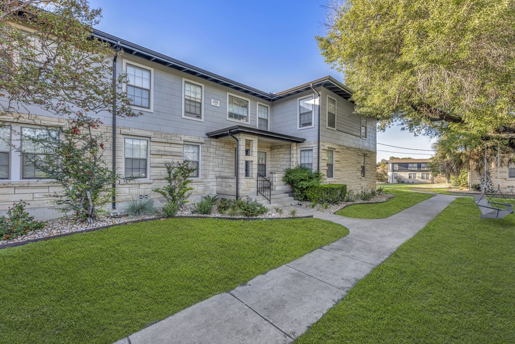 a sidewalk in front of a building with grass and trees  at Sunset Ridge, San Antonio, 78209
