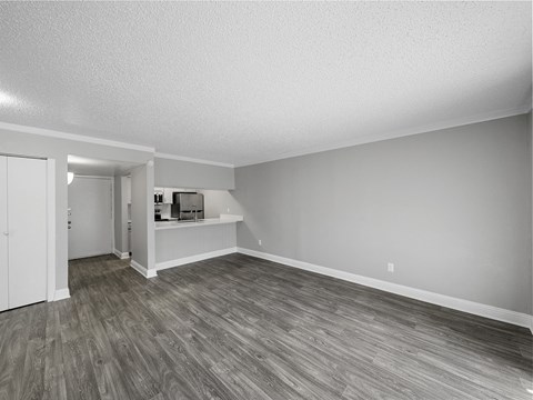 an empty living room with wood flooring and a kitchen