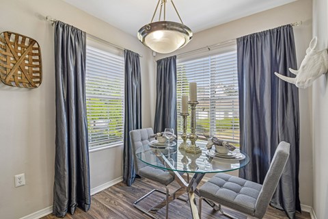 A dining room with a glass table and grey chairs.