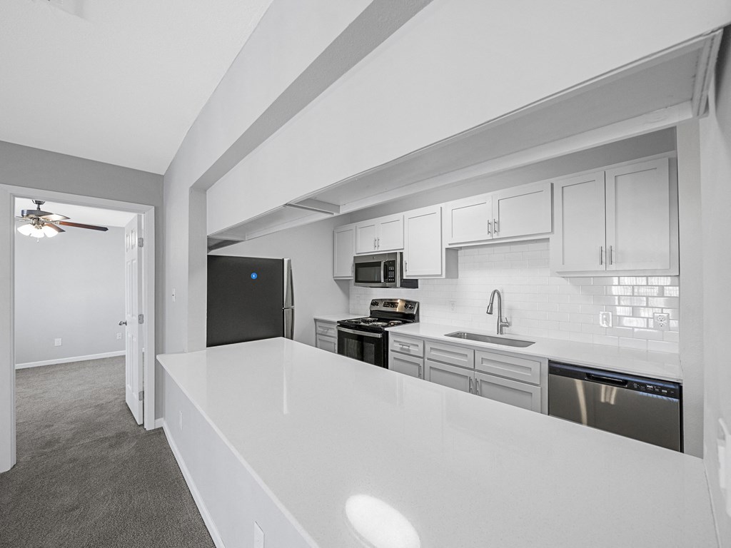a white kitchen with a white counter top and black appliances
