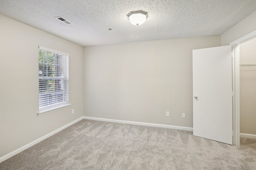 A room with a carpeted floor, a window with blinds, and a white door.