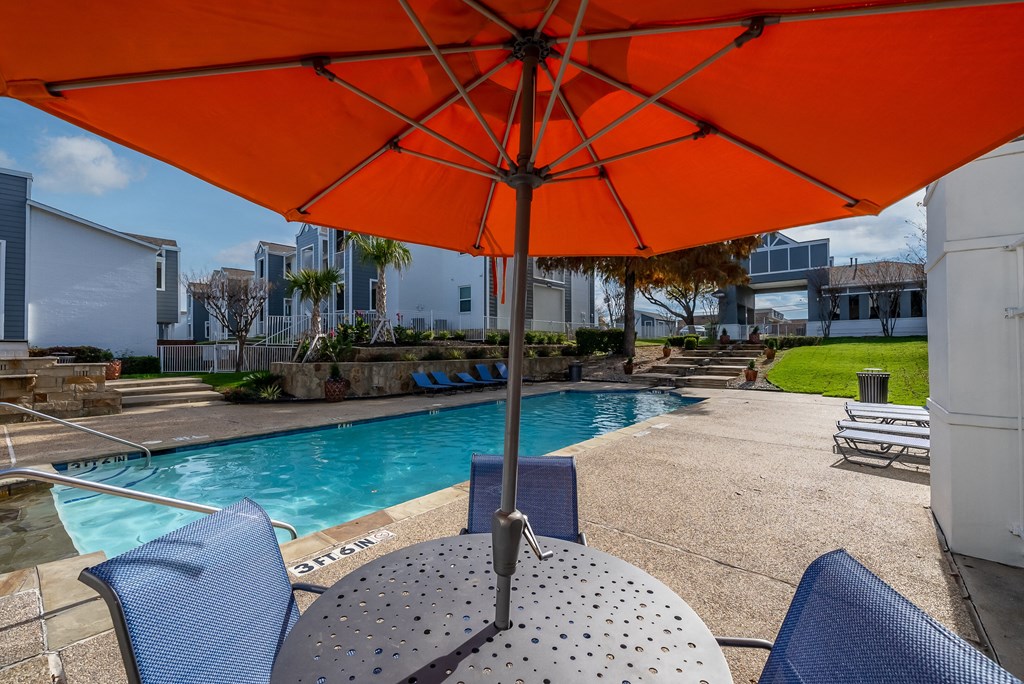 a pool with an orange umbrella over a table with chairs