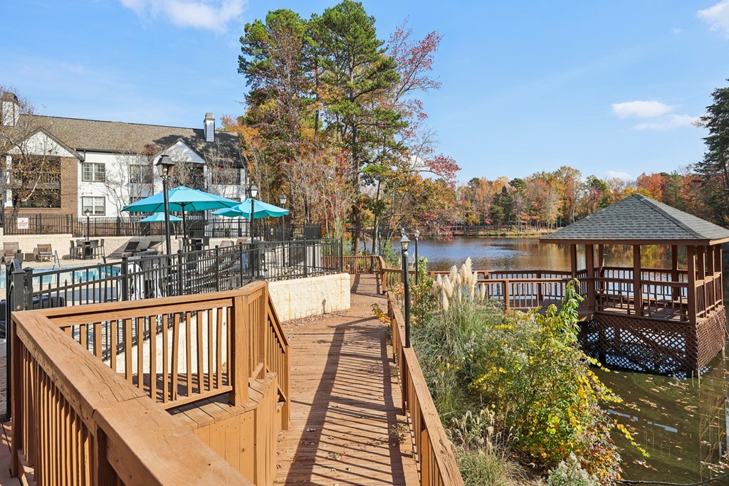 A wooden deck overlooks a body of water with a gazebo and trees in the background.