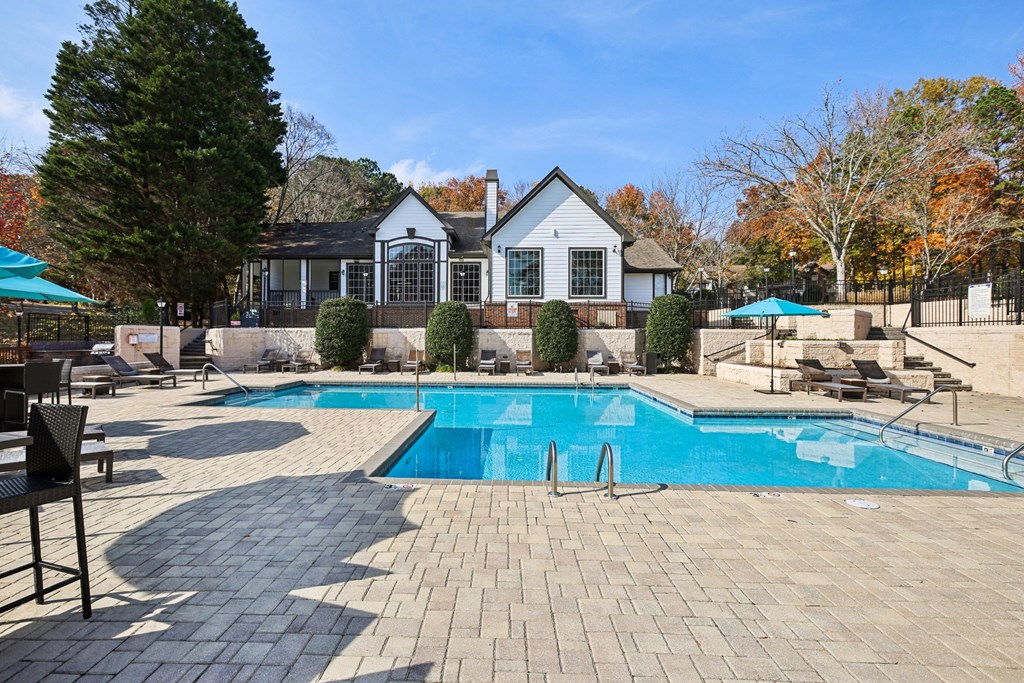 A pool surrounded by a brick patio and a house in the background.