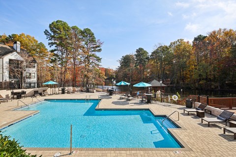 A large outdoor swimming pool surrounded by trees and a building.