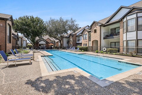 A swimming pool surrounded by apartment buildings and lounge chairs.